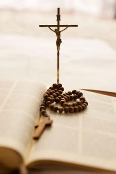 Focused close-up of a rosary and Bible with a crucifix in the background, symbolizing faith.