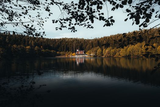 Peaceful autumn scene of Karagöl lake reflecting a forest and house, perfect for nature lovers.