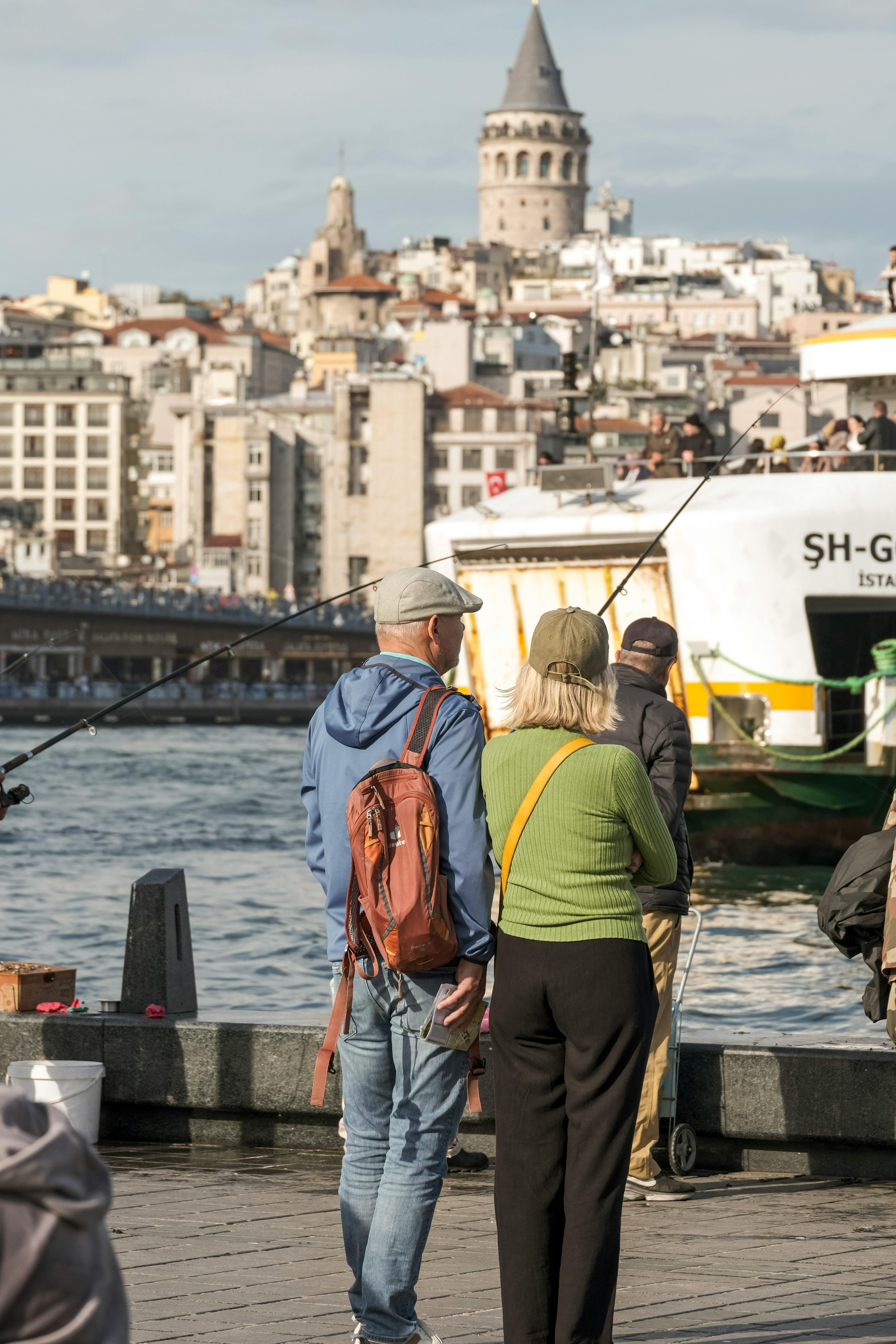 Gratuit Un couple d'âge moyen fait du tourisme près de la tour de Galata à Istanbul avec un ferry qui passe. Photos