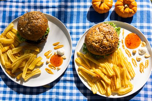 Free Delicious gourmet burgers with fries on a checkered cloth, perfect for a casual meal setting. Stock Photo