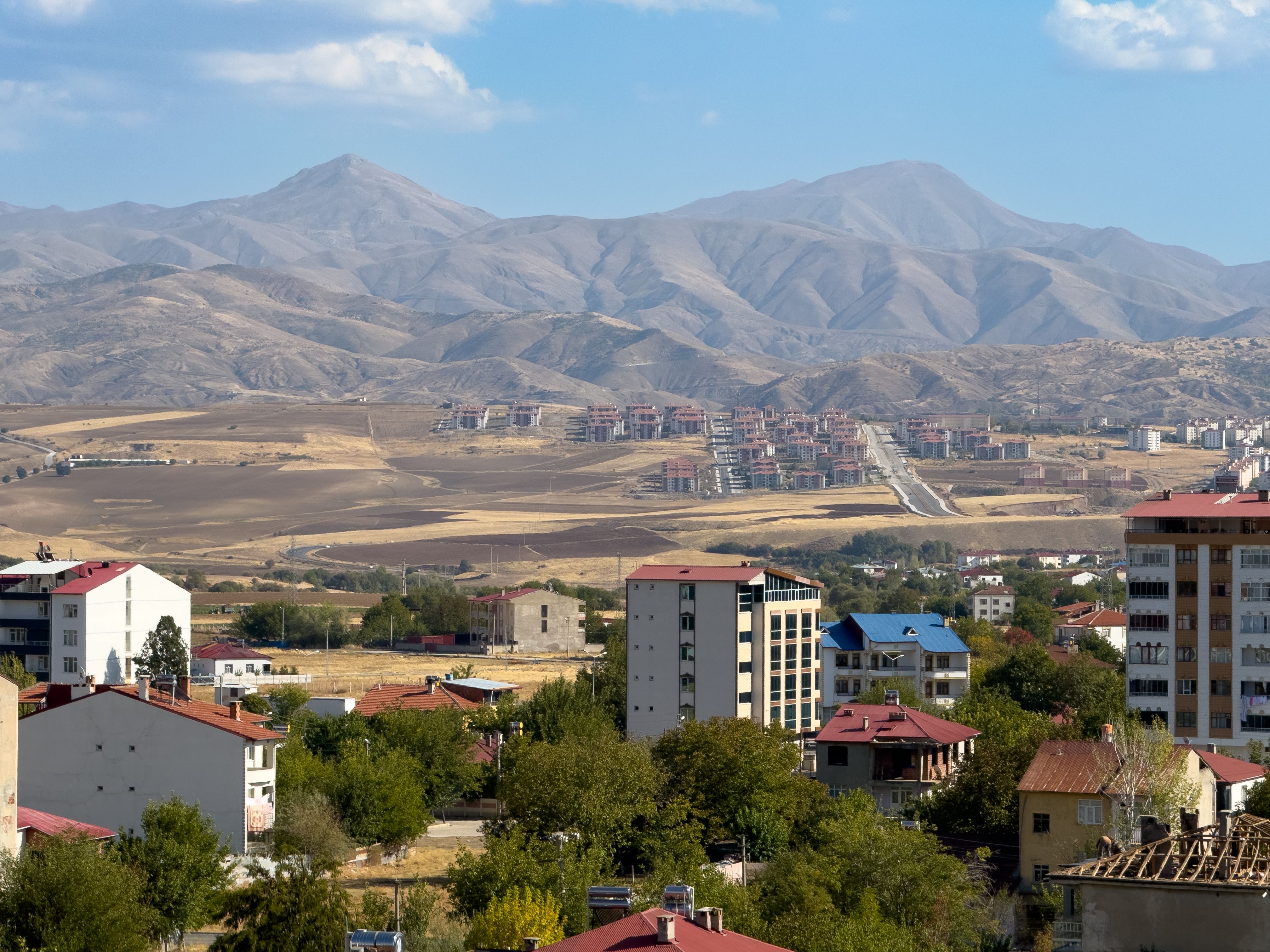 A picturesque landscape of Kovancılar, Türkiye, with mountains and residential buildings under a bright sky.
