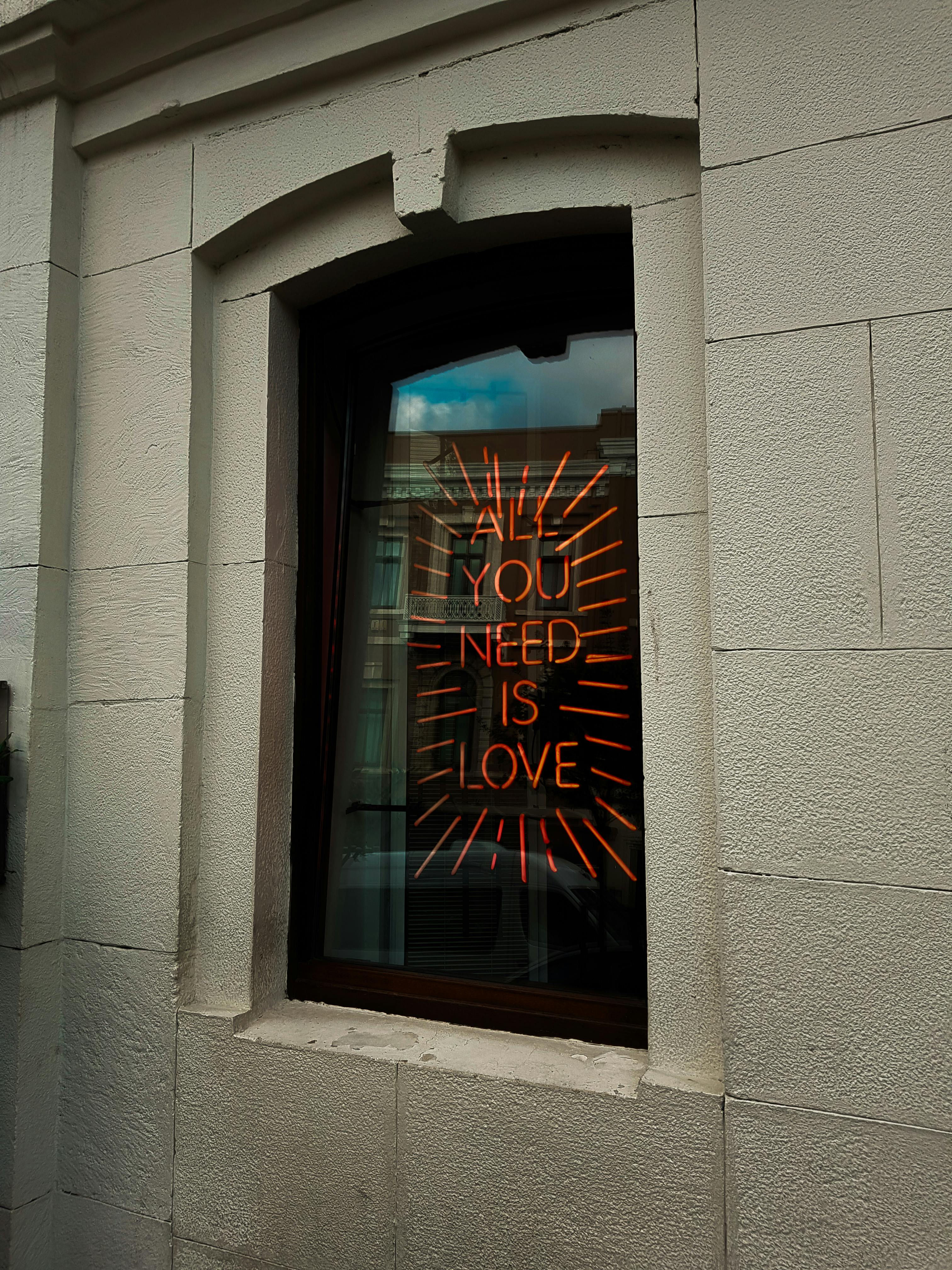 A glowing neon sign displaying "All You Need Is Love" in a window, embodying warmth and positive vibes.