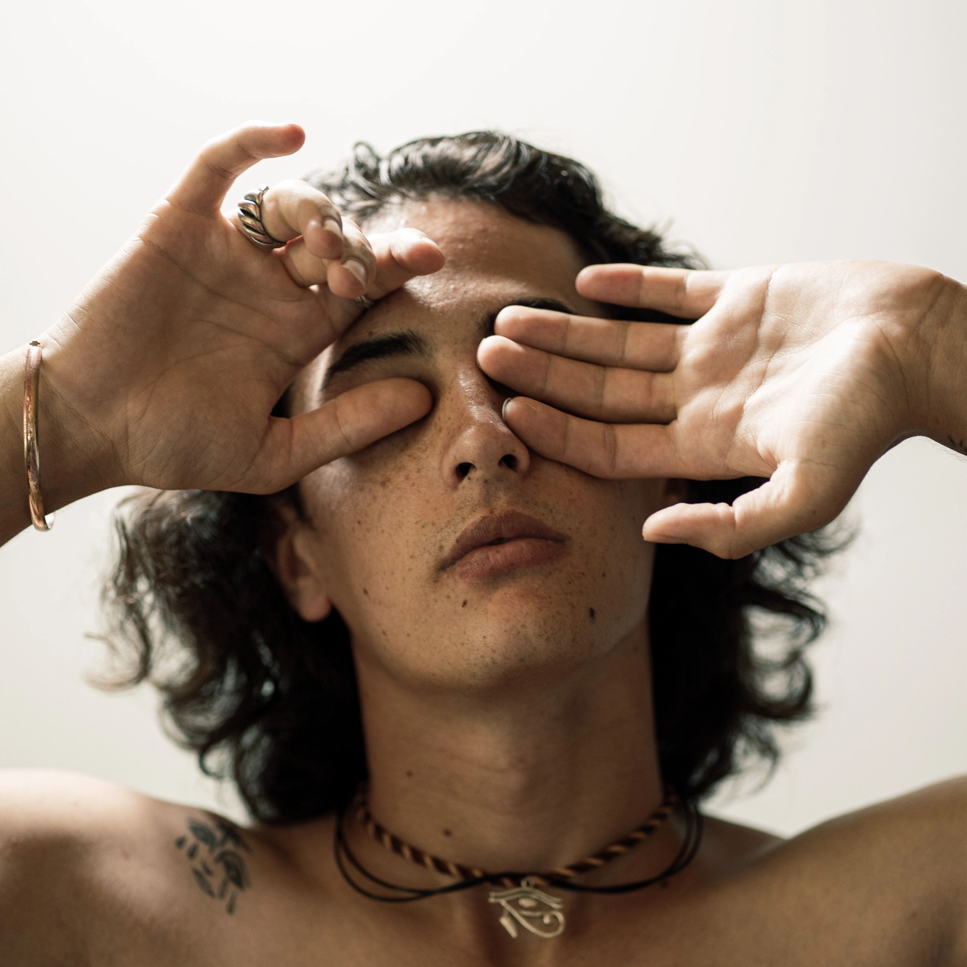 A contemplative portrait of a young man covering his eyes with an artistic pose.