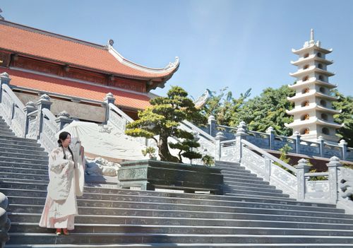Free Woman in traditional dress on temple steps with pagoda and bonsai tree. Stock Photo