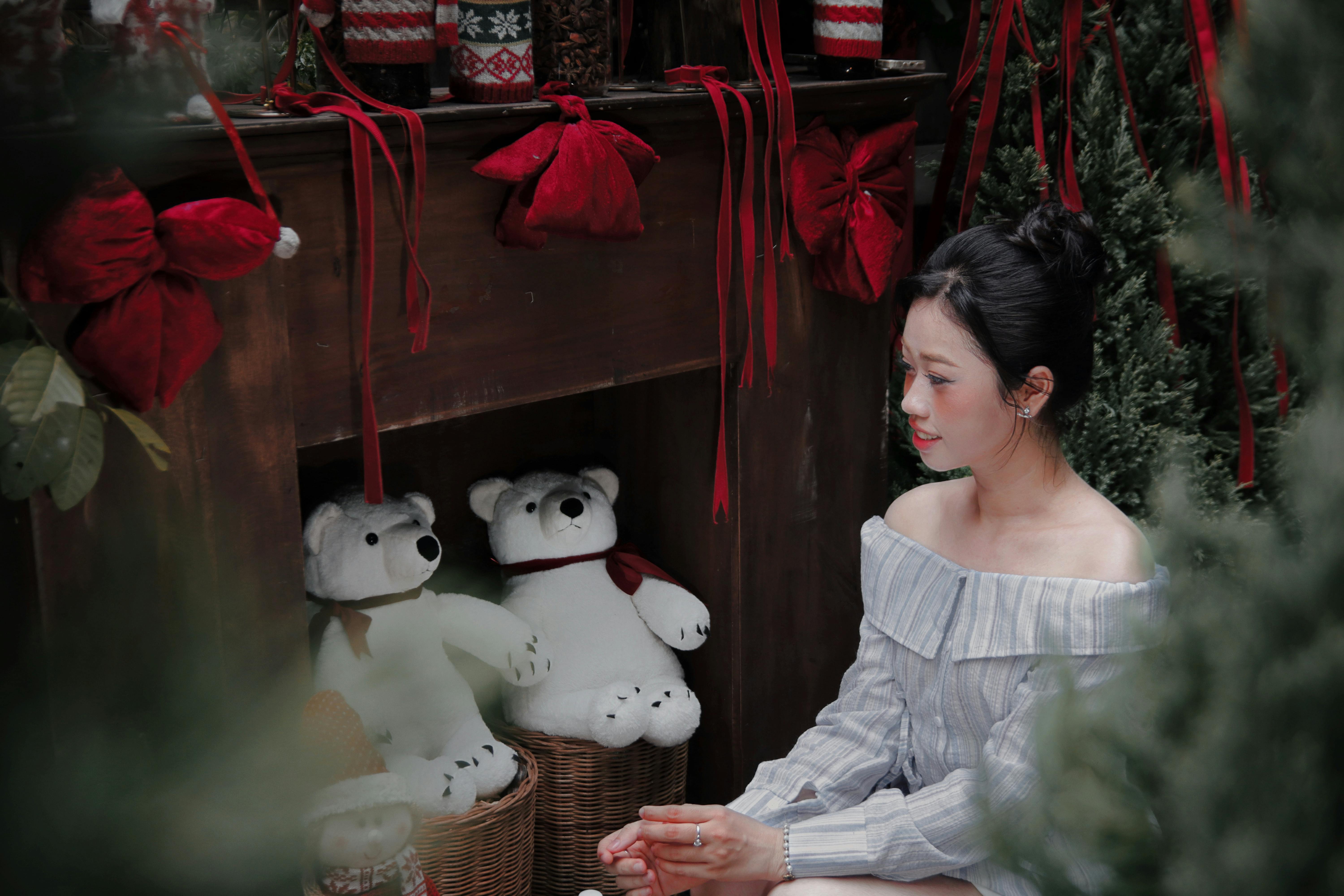 A woman admires a Christmas fireplace setup with teddy bears and red decorations indoors.
