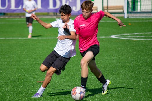 Two teenage soccer players competing aggressively on the field.