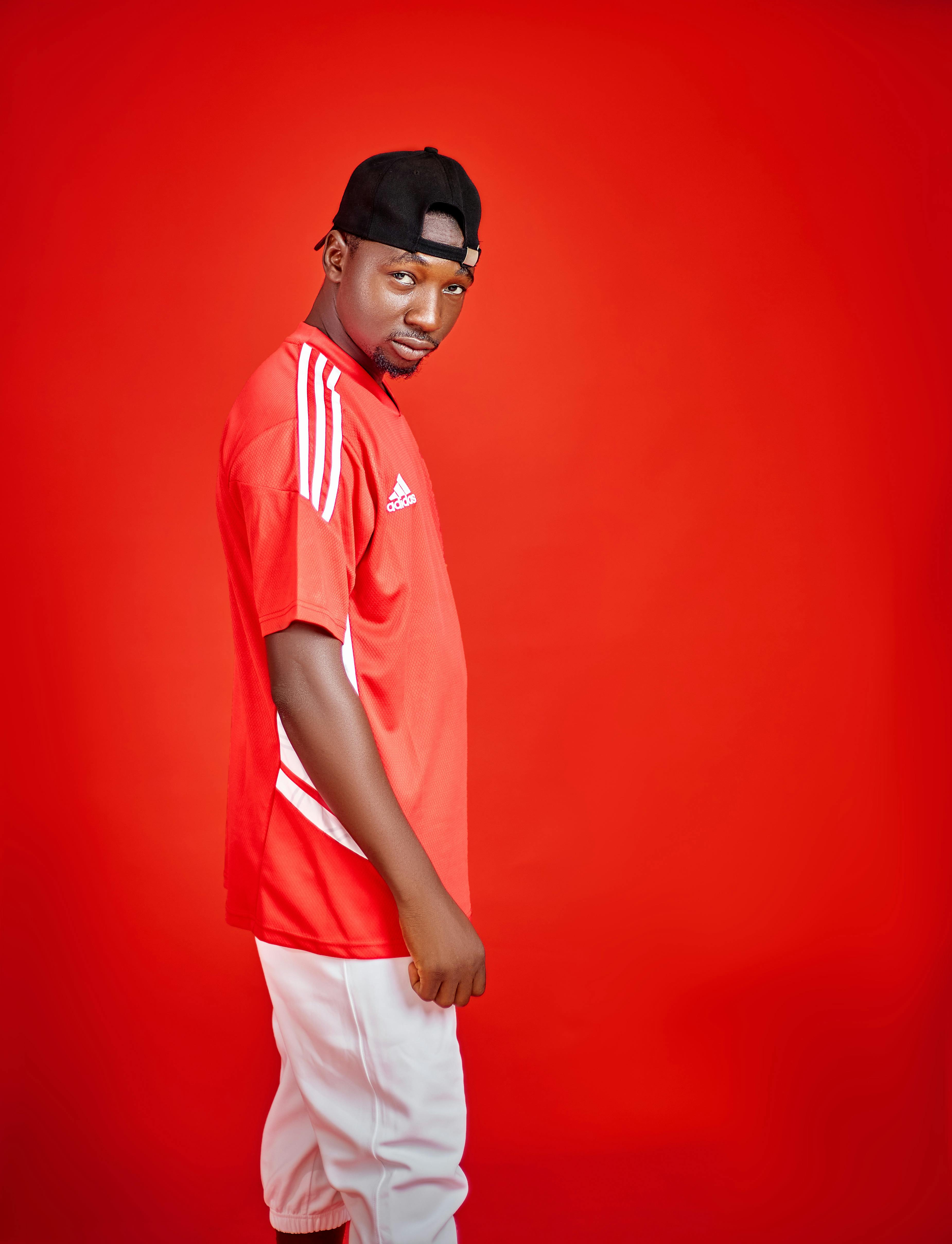 Confident male model wearing red sports jersey and cap against vibrant red backdrop.