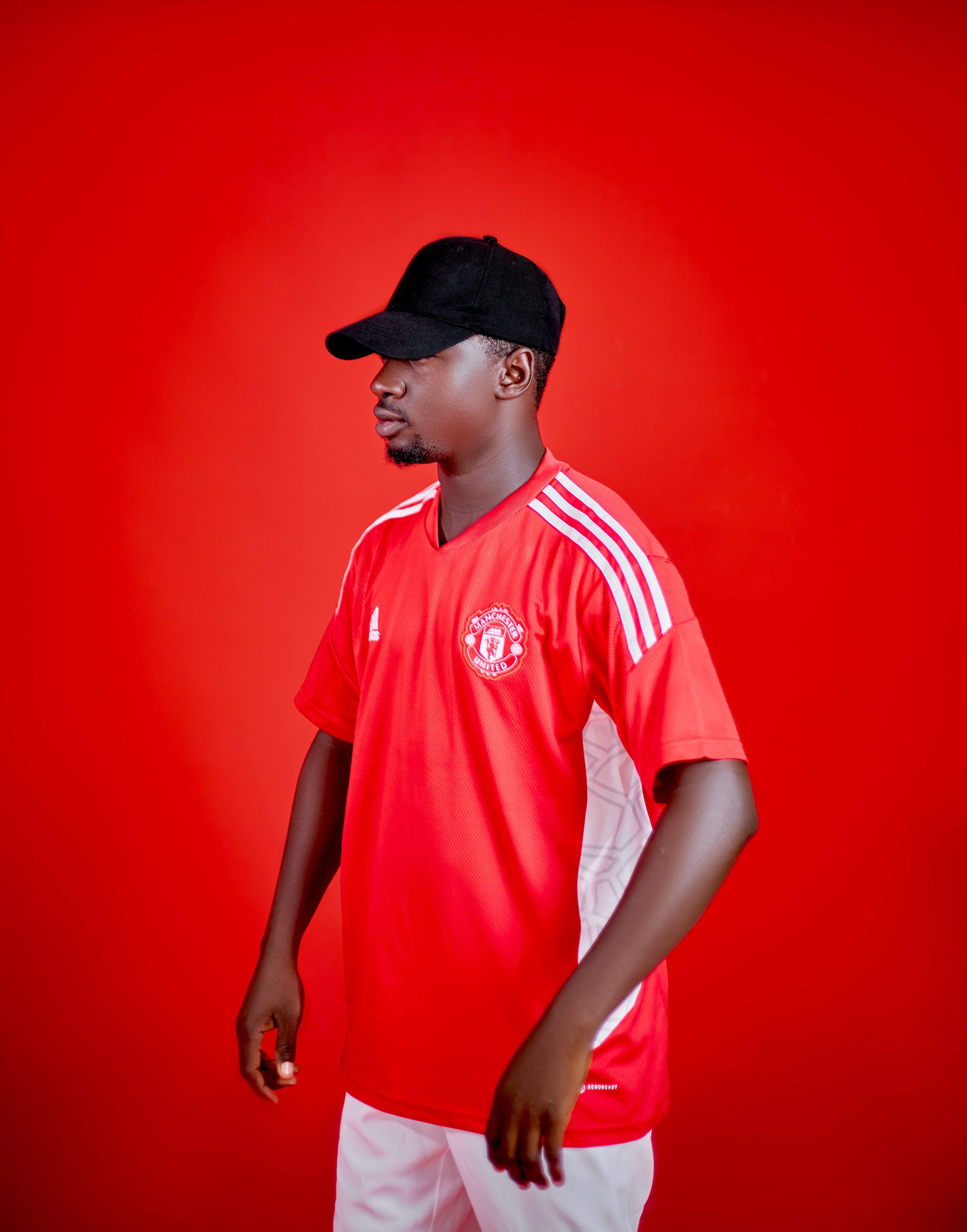 Man wearing a red soccer jersey and black cap stands against a red background.