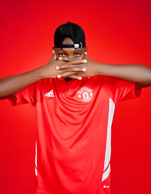 Free A man in a red jersey poses with hands covering his face against a vivid red backdrop. Stock Photo