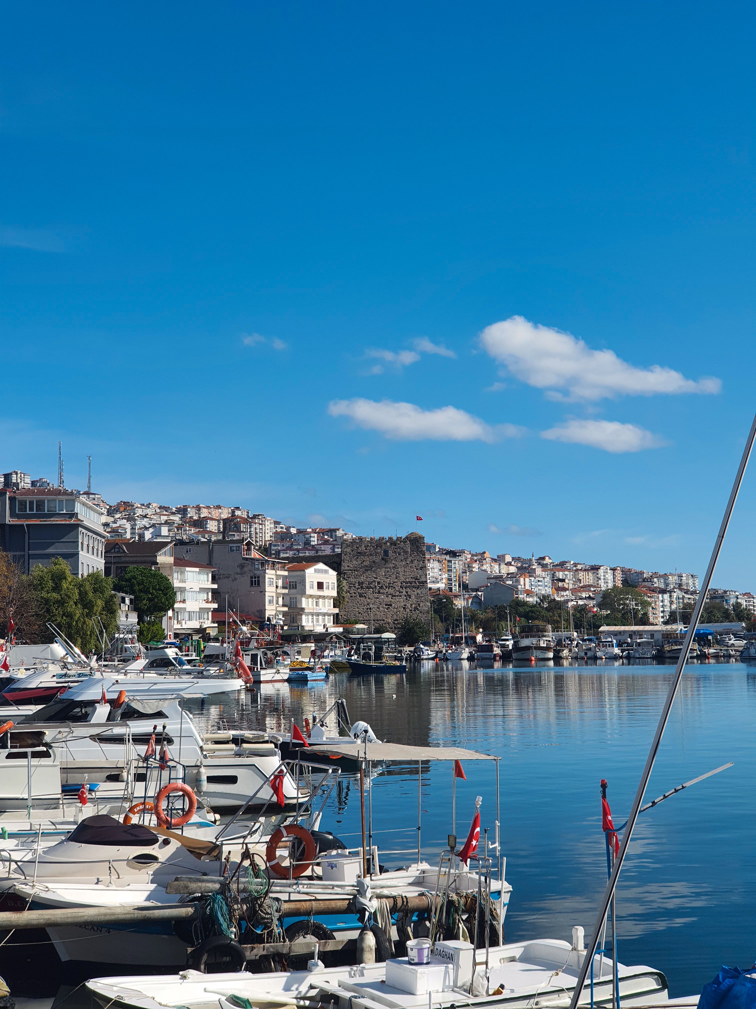 A vibrant coastal scene featuring a marina and town under a clear blue sky in Sinop, Turkey.