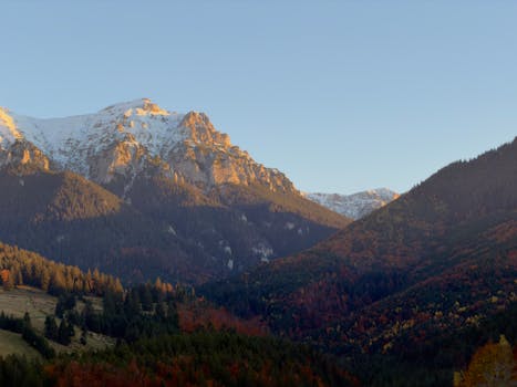 Captivating autumn scene of the Bucegi Mountains with vibrant fall foliage and snow-capped peaks at sunset.