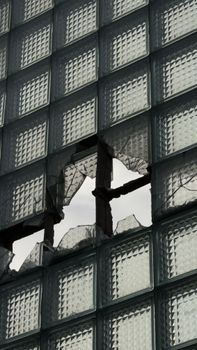 Shattered glass panel in a grid facade, revealing the sky through broken sections.
