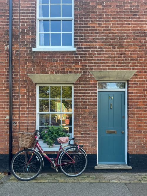 Free A quaint red brick house facade in Southwold, UK, featuring a blue door and a parked bicycle. Stock Photo