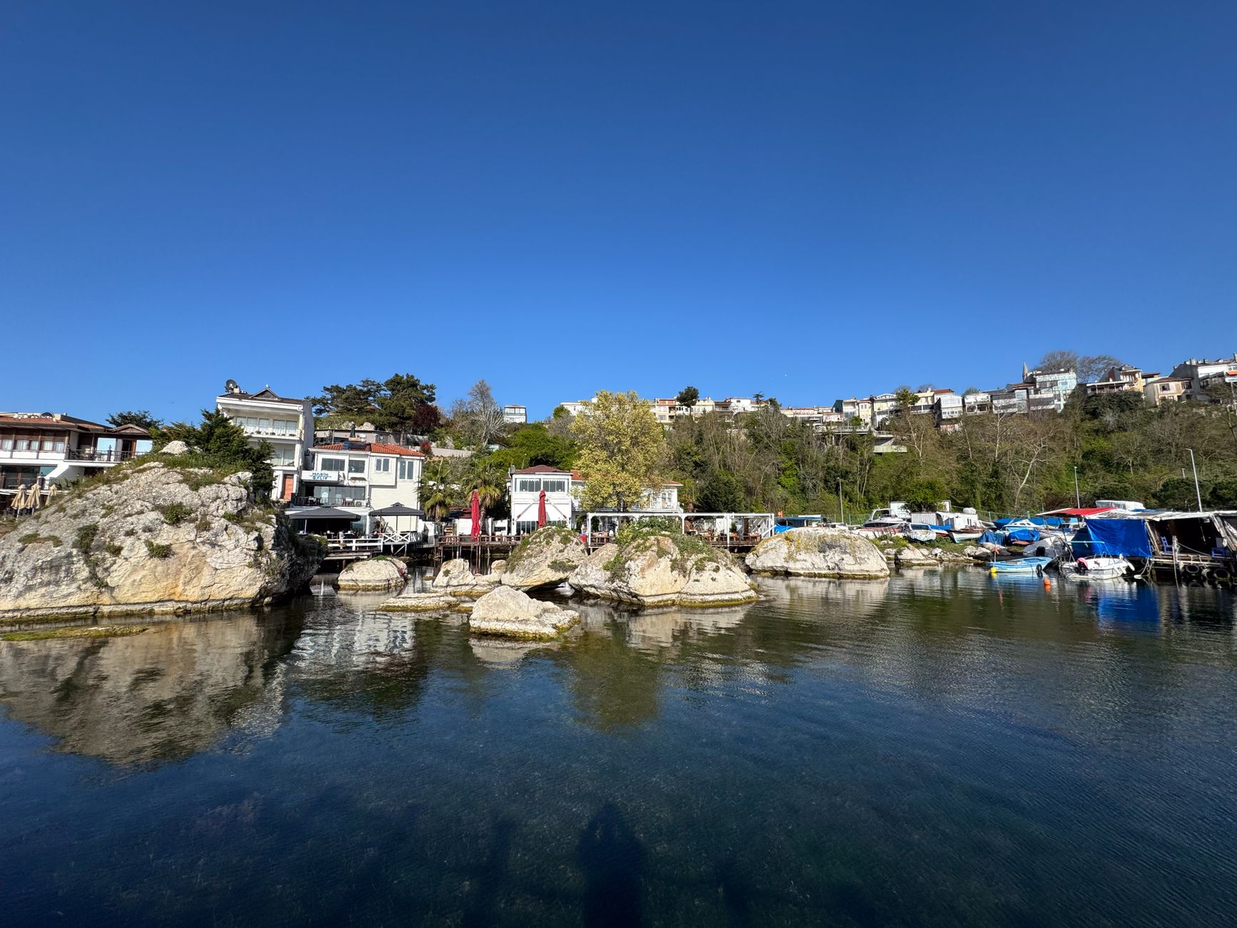 A picturesque waterfront scene with houses, rocky shoreline, and clear blue skies.