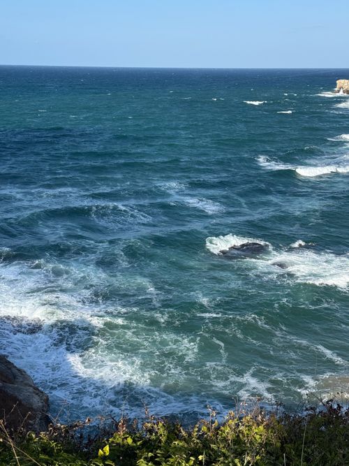 Free Captivating view of ocean waves crashing on a rocky shoreline under a bright blue sky. Perfect for nature and travel themes. Stock Photo