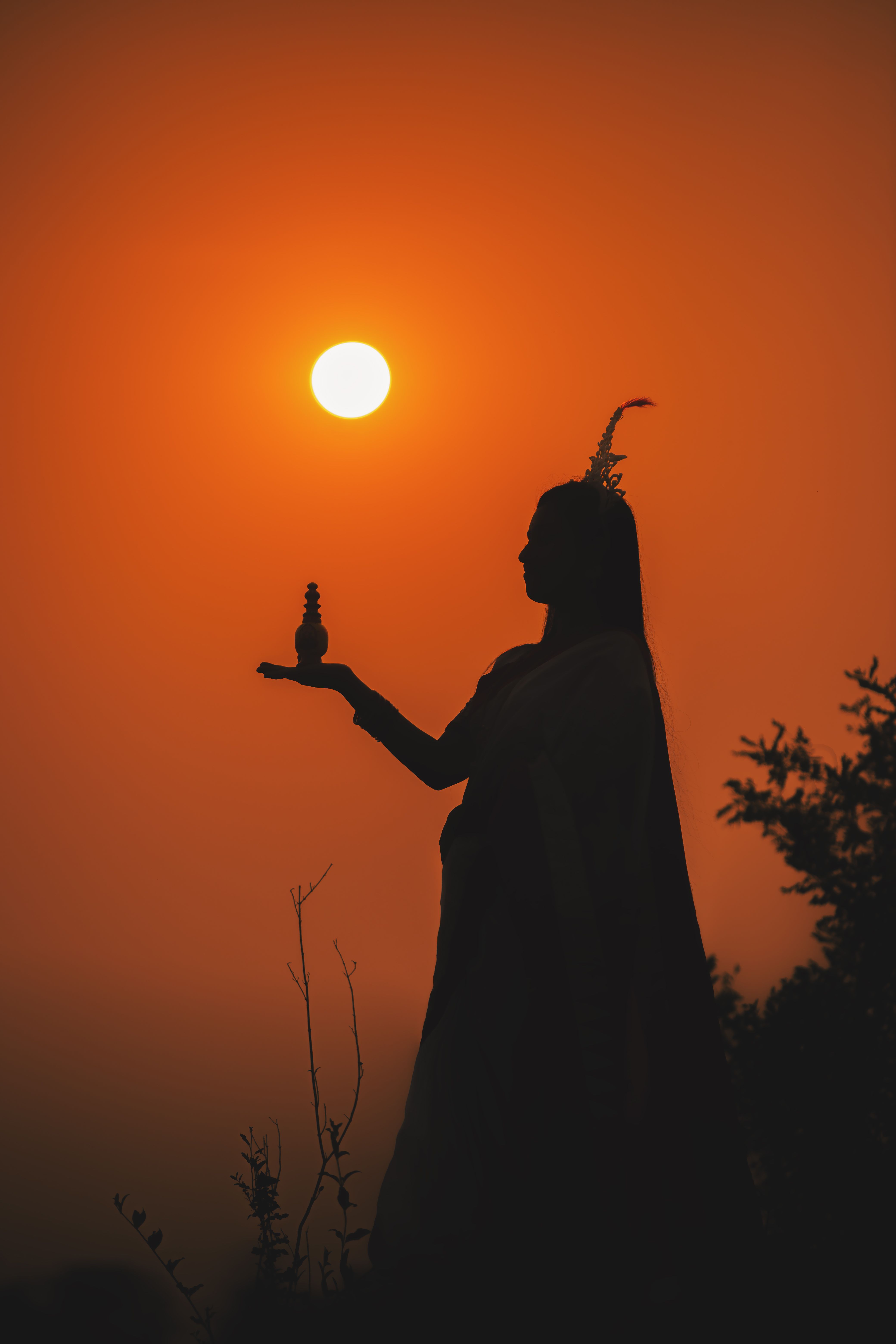 Silhouette of a woman holding a figurine against a vivid sunset backdrop.. silhouette, woman, holding