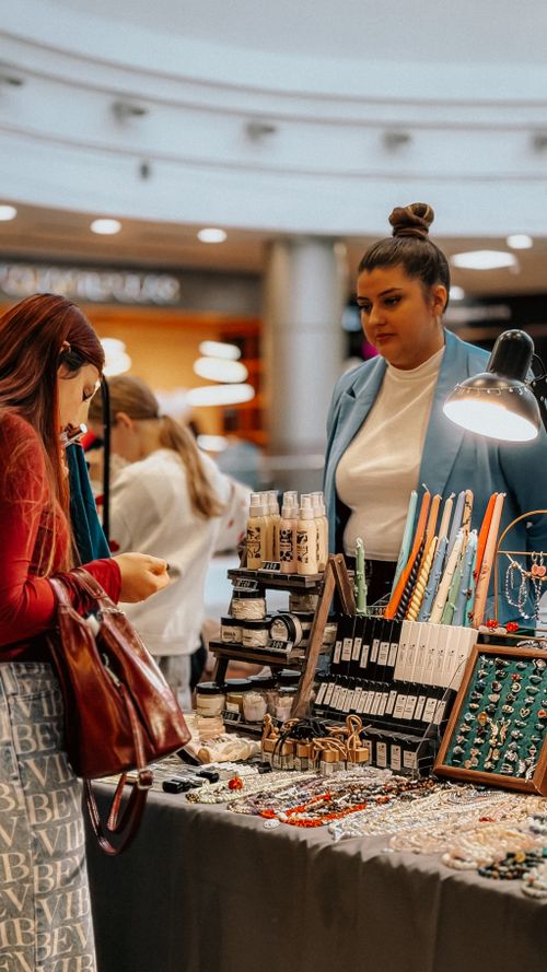 Free Women browsing handmade jewelry at indoor market stall. Stock Photo