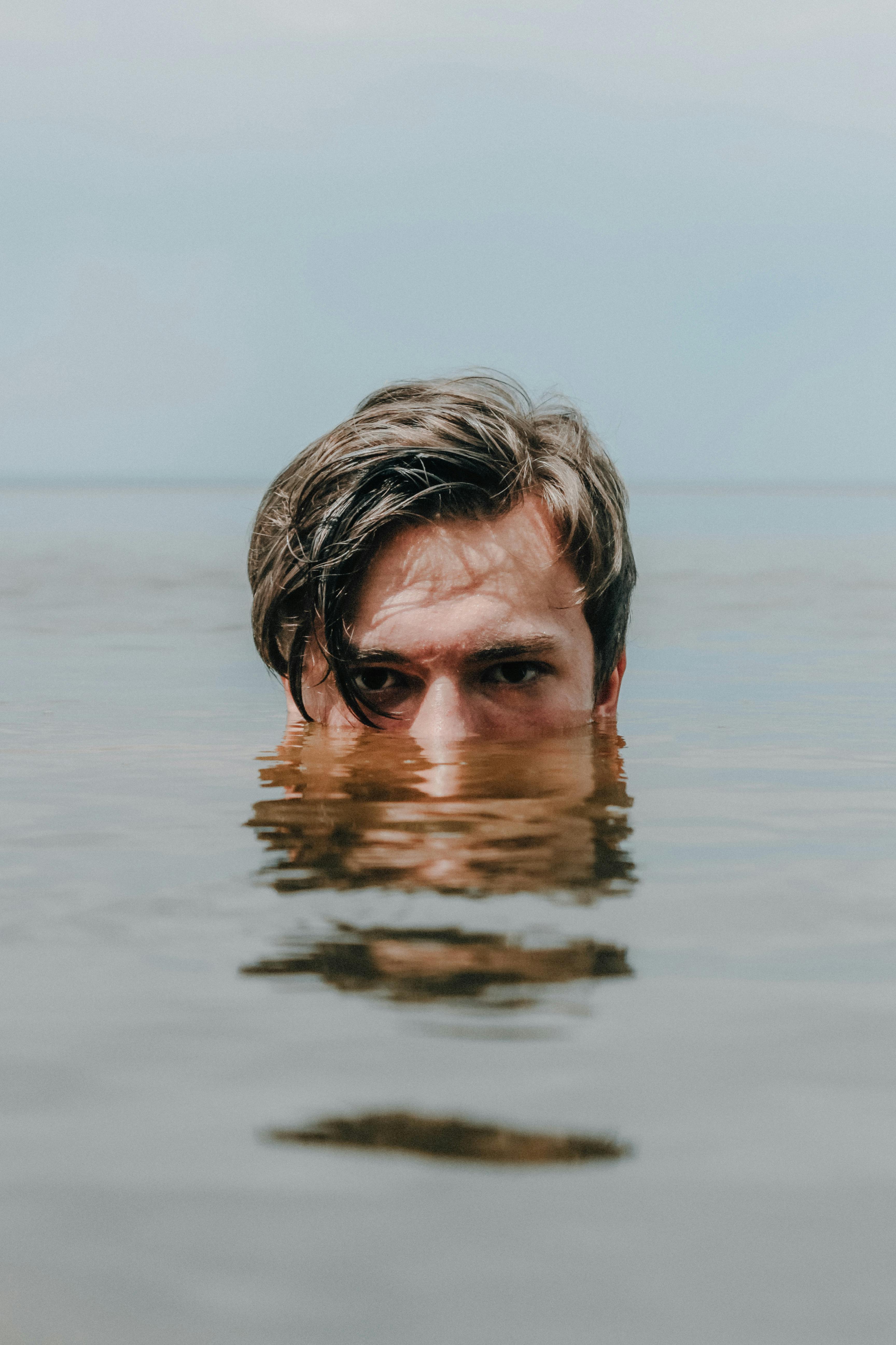 Kostnadsfria Ett lugnt och spännande porträtt av en man delvis nedsänkt i vatten med en reflekterande yta. Stock foto