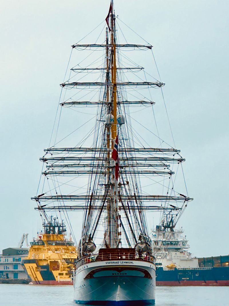 Tall ships with masts moored along a crowded riverbank quay at the Armada de Rouen
