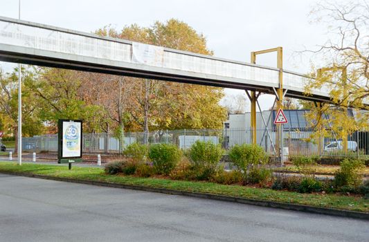 Elevated pedestrian bridge over a road in Compiègne, France, framed by vibrant autumn foliage.