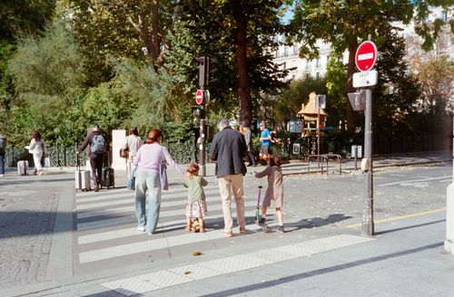 Free A family crossing the street in Paris on a sunny day, surrounded by greenery. Stock Photo