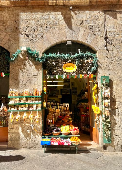 Free A colorful Italian grocery store showcasing fresh fruits and local products under an arched stone entrance. Stock Photo