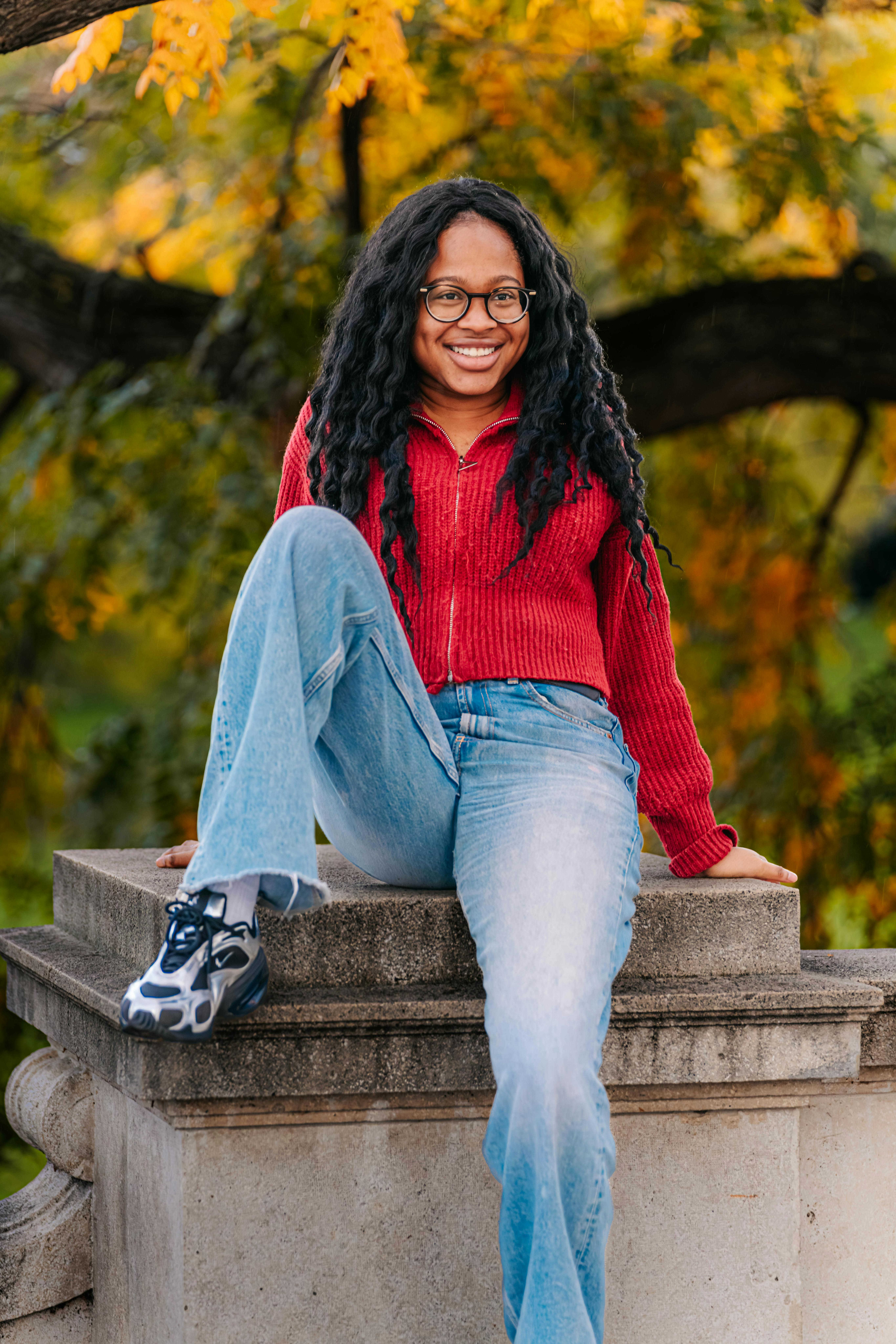 Free A joyful young woman sits on a ledge with autumn leaves in Vienna, Austria. Stock Photo