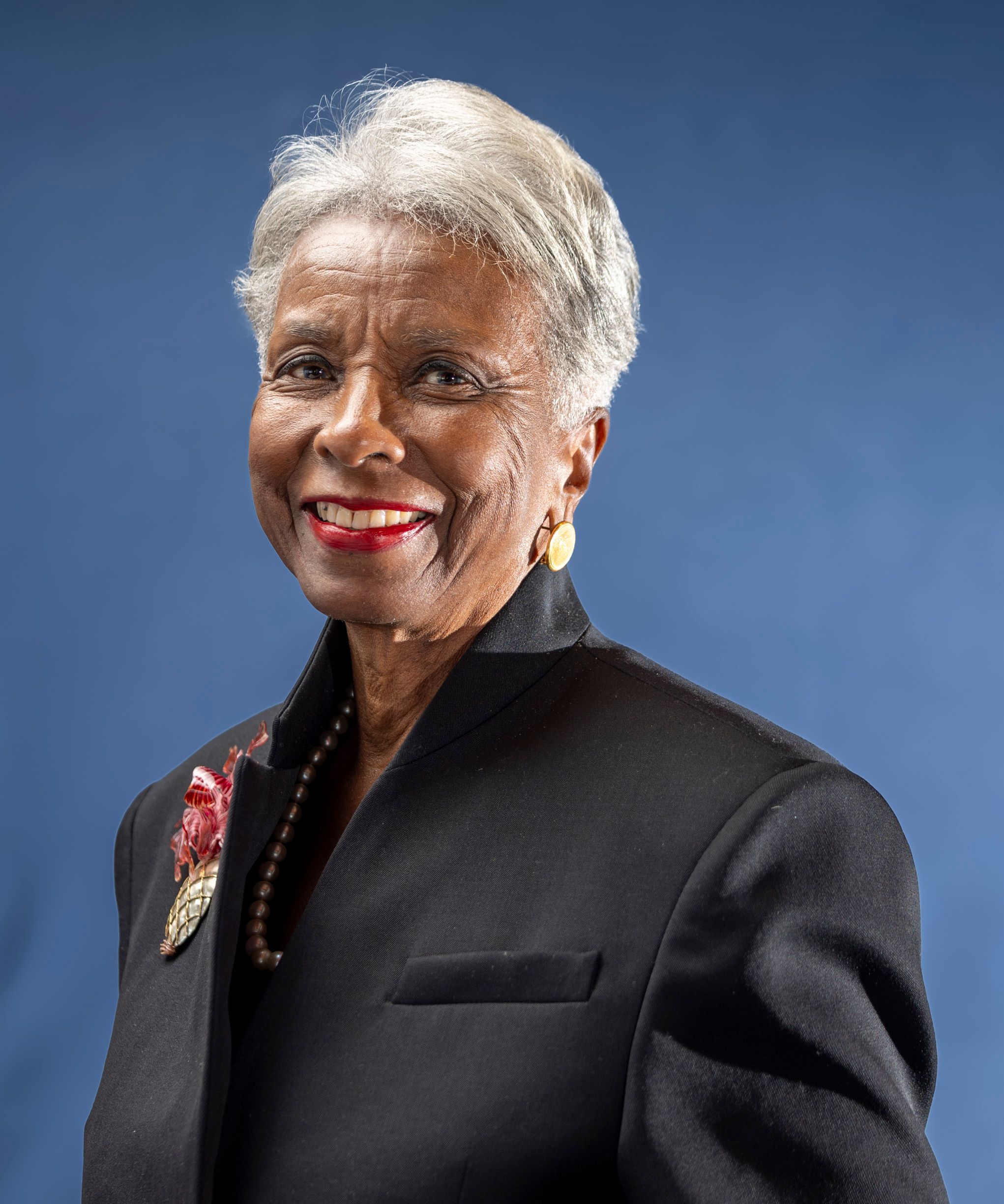 Portrait of a smiling senior woman in a dark suit, against a blue backdrop.