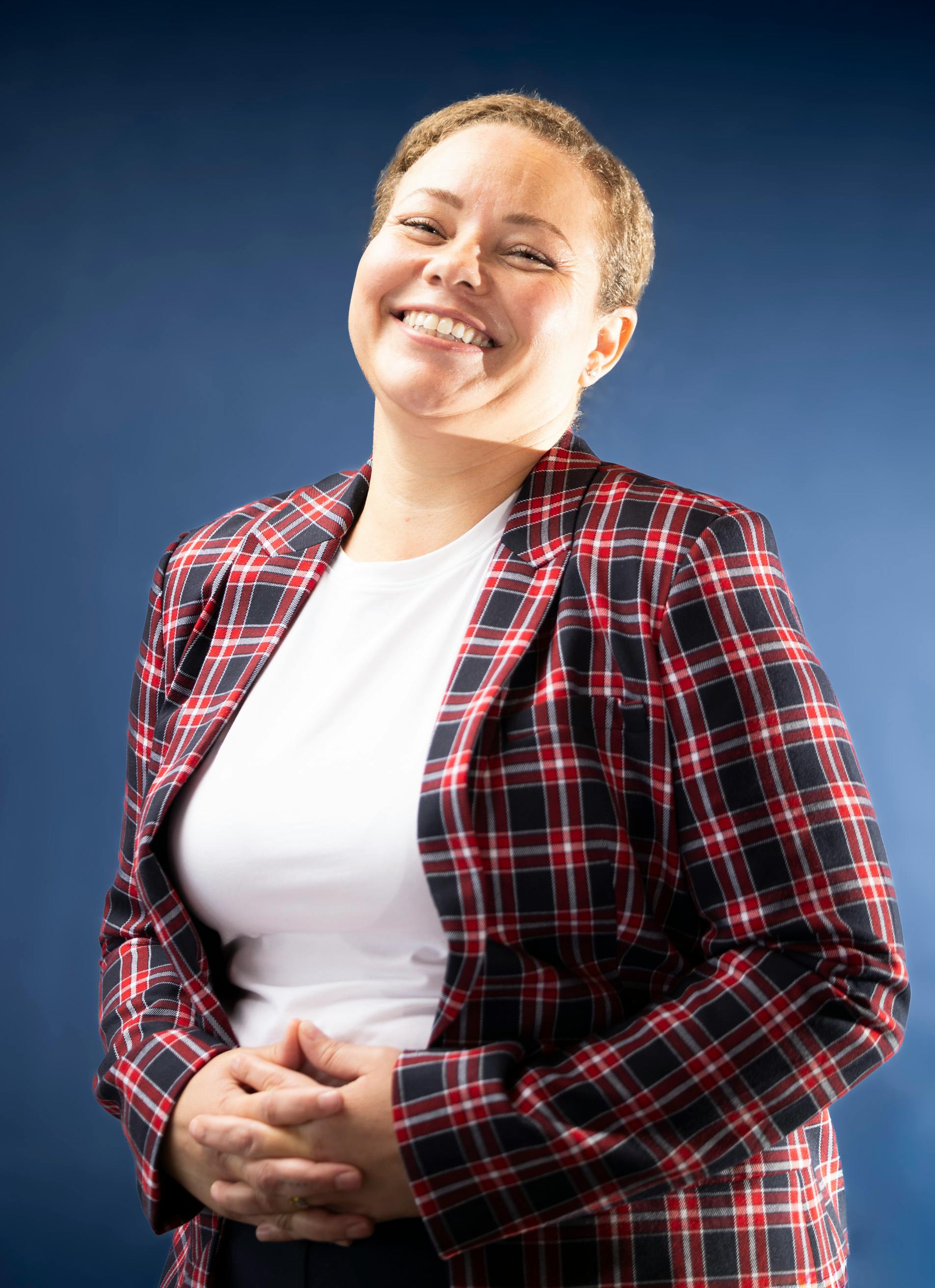 Smiling woman in a red plaid blazer, posing against a blue studio background.