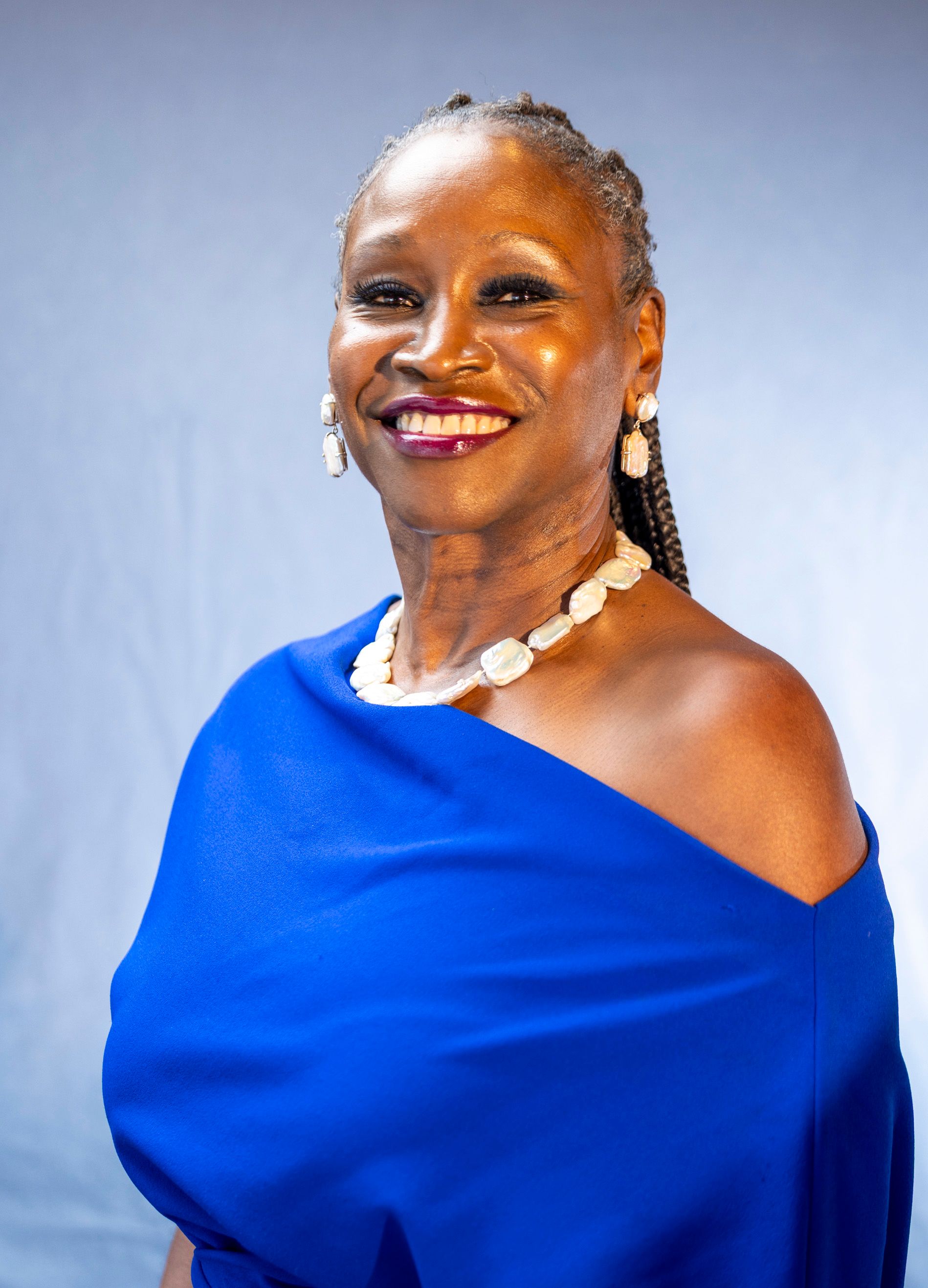 An elegant senior woman smiling in a blue dress against a soft background.