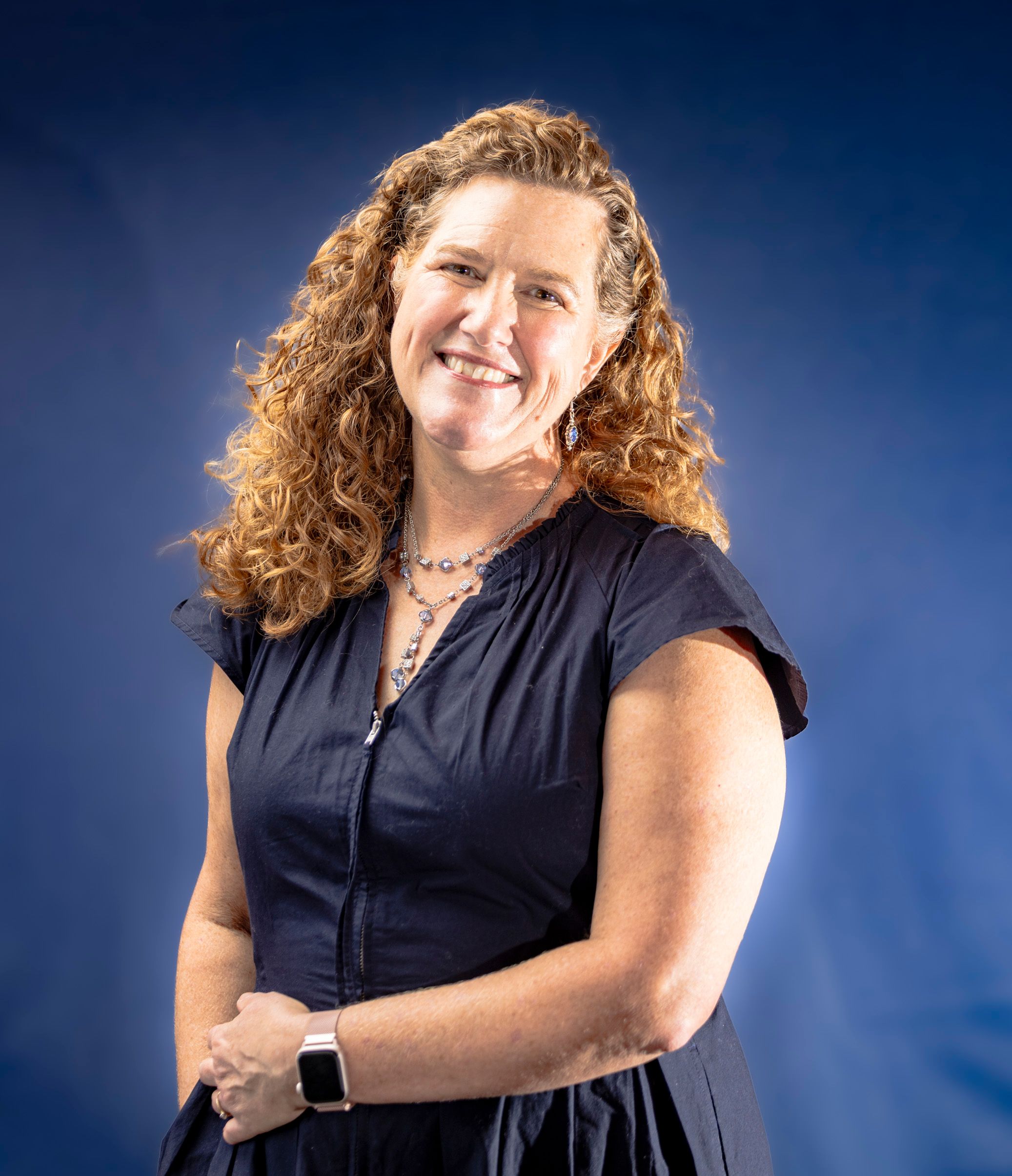 Portrait of a smiling woman in a blue dress against a blue background, exuding warmth.