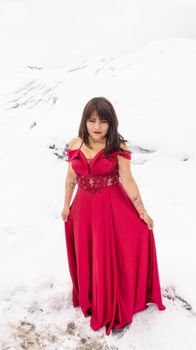 A woman in a vibrant red dress poses gracefully in a snowy landscape, creating a striking contrast.