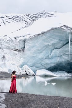 A woman in a red dress stands by a glacier, creating a striking contrast in nature.