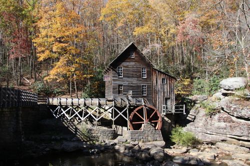 Free Old wooden watermill surrounded by vibrant autumn foliage in forest. Stock Photo