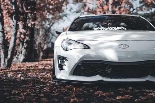 Free Close-up of a white car parked on a leaf-covered path in fall, showcasing modern design. Stock Photo