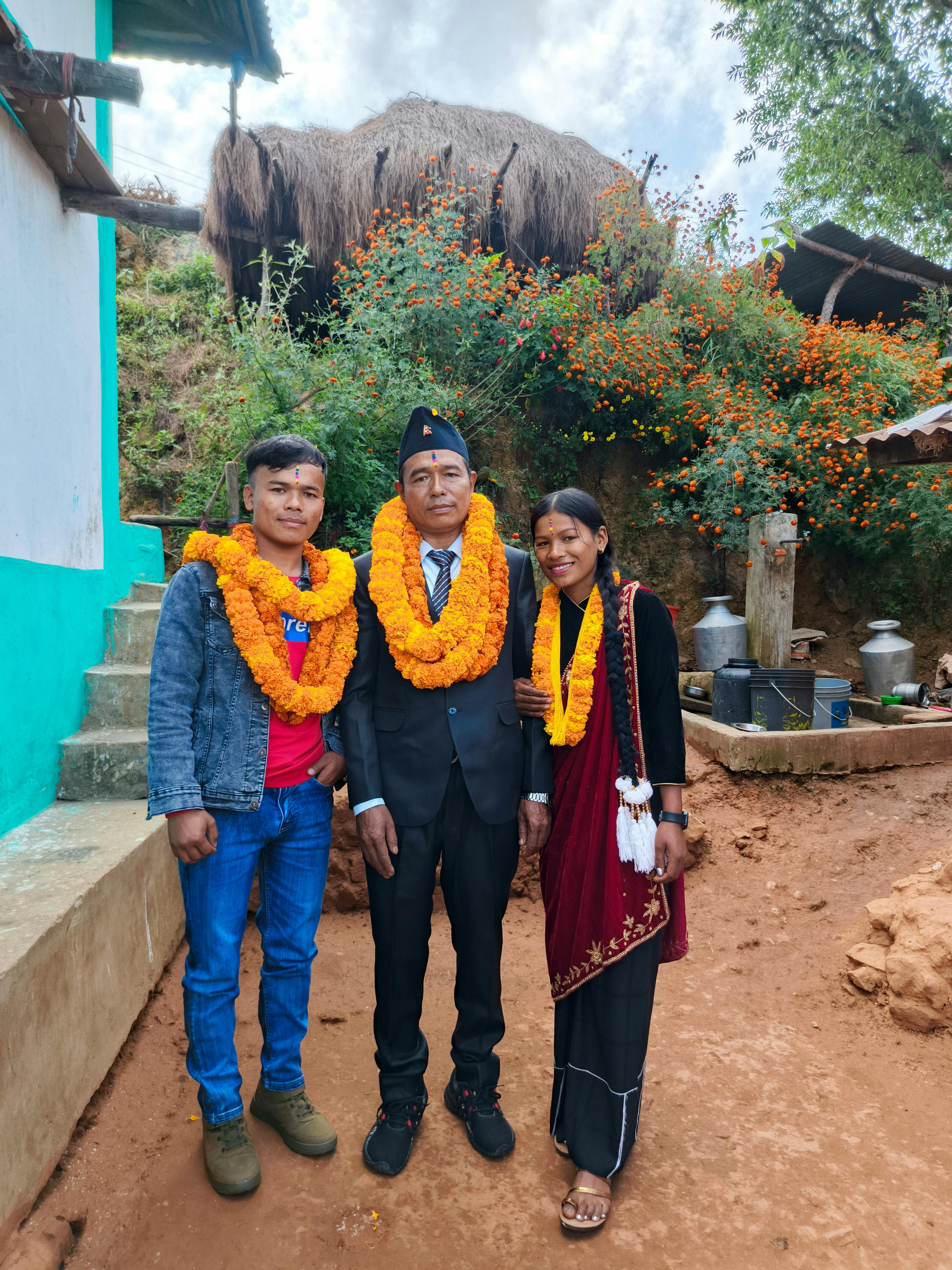 A Nepali family in traditional attire wearing marigold garlands outside their home.