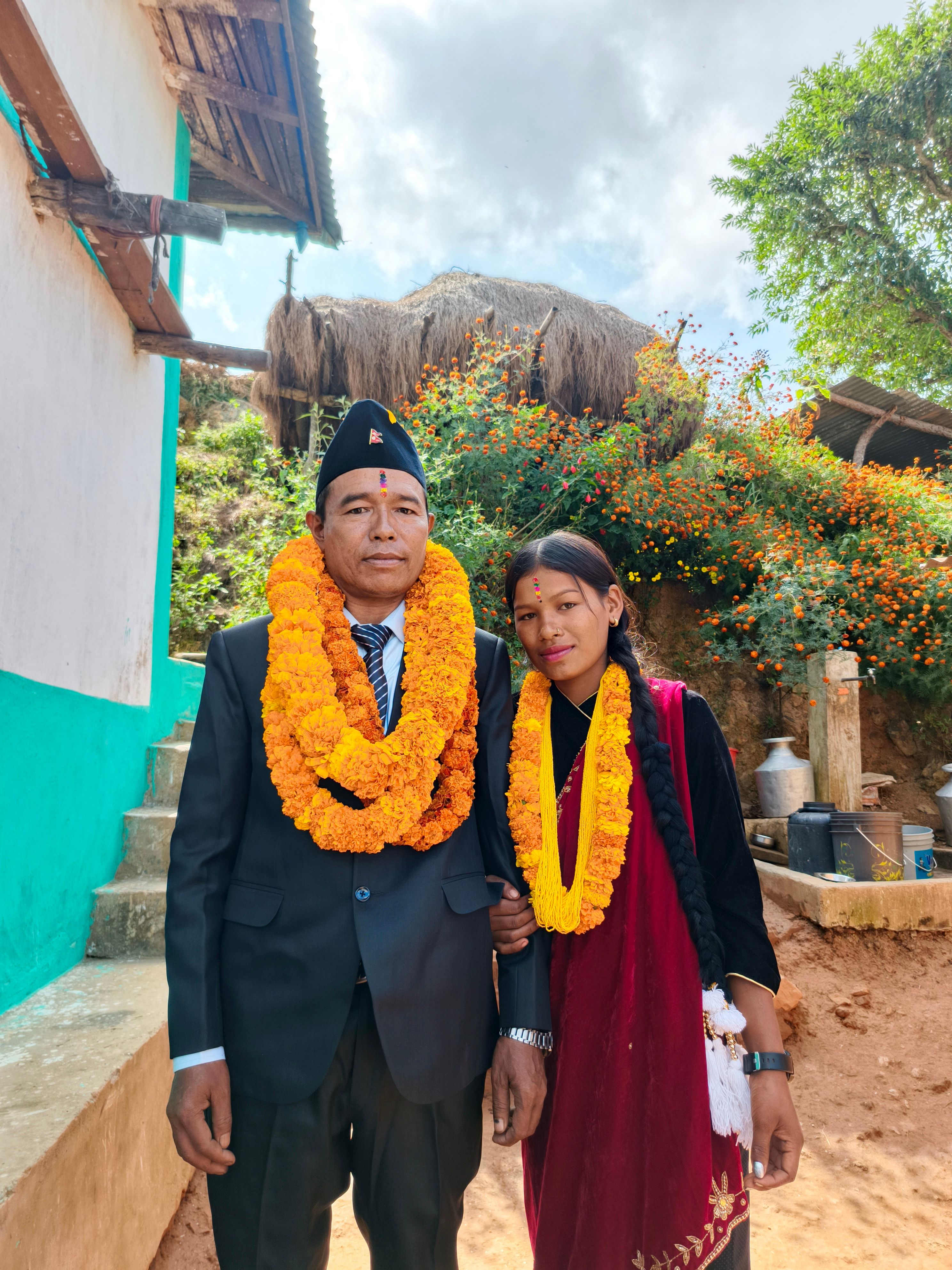 Smiling Nepali couple wearing garlands in traditional attire outdoors, celebrating a festival.