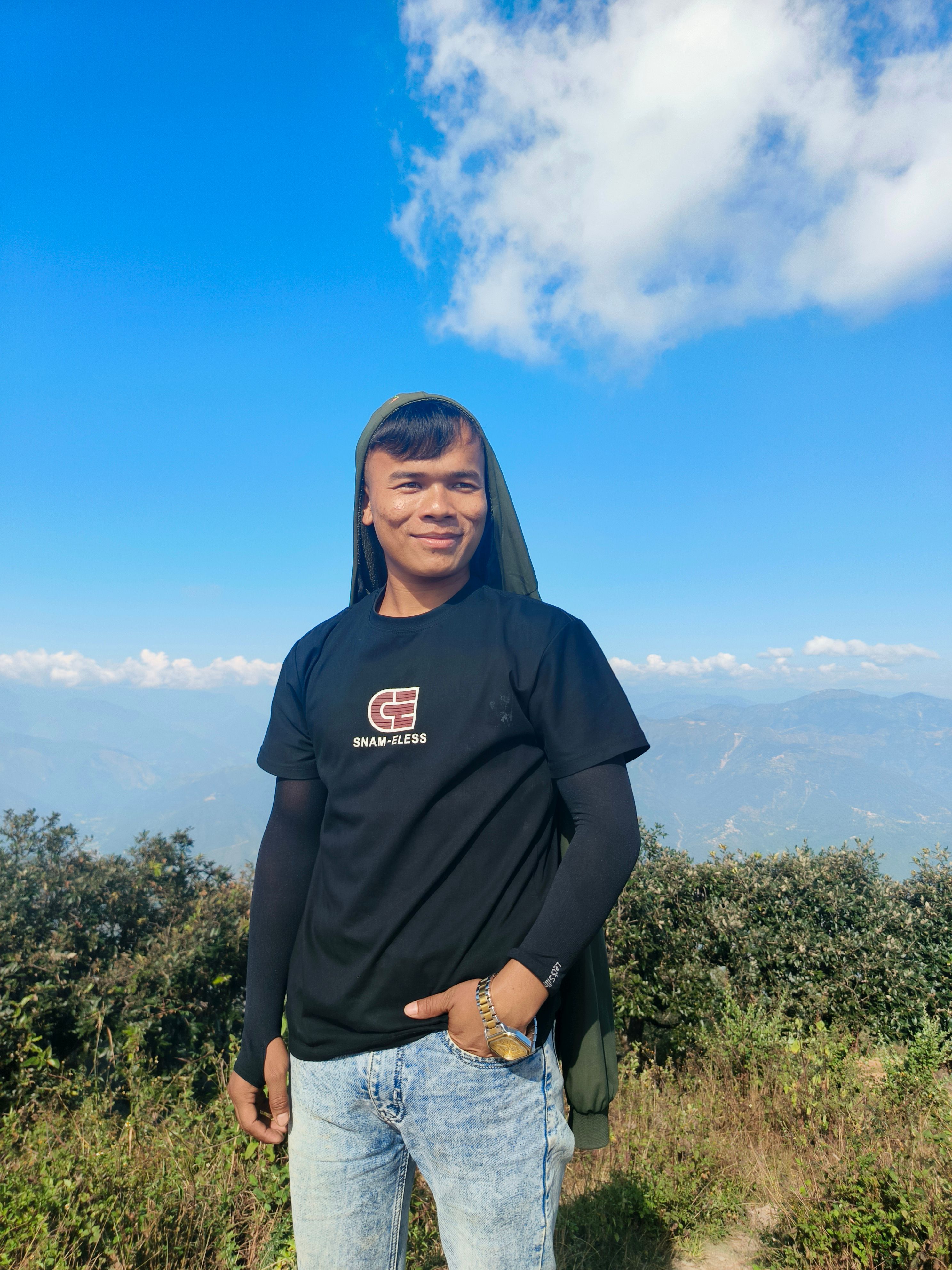 A smiling person enjoys a sunny day outdoors with a scenic mountain background.