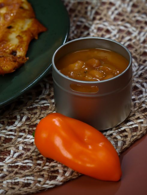 A glass hot sauce bottle filled with smooth orange-colored habanero carrot sauce next to whole habanero peppers and a halved lime on a wood board.