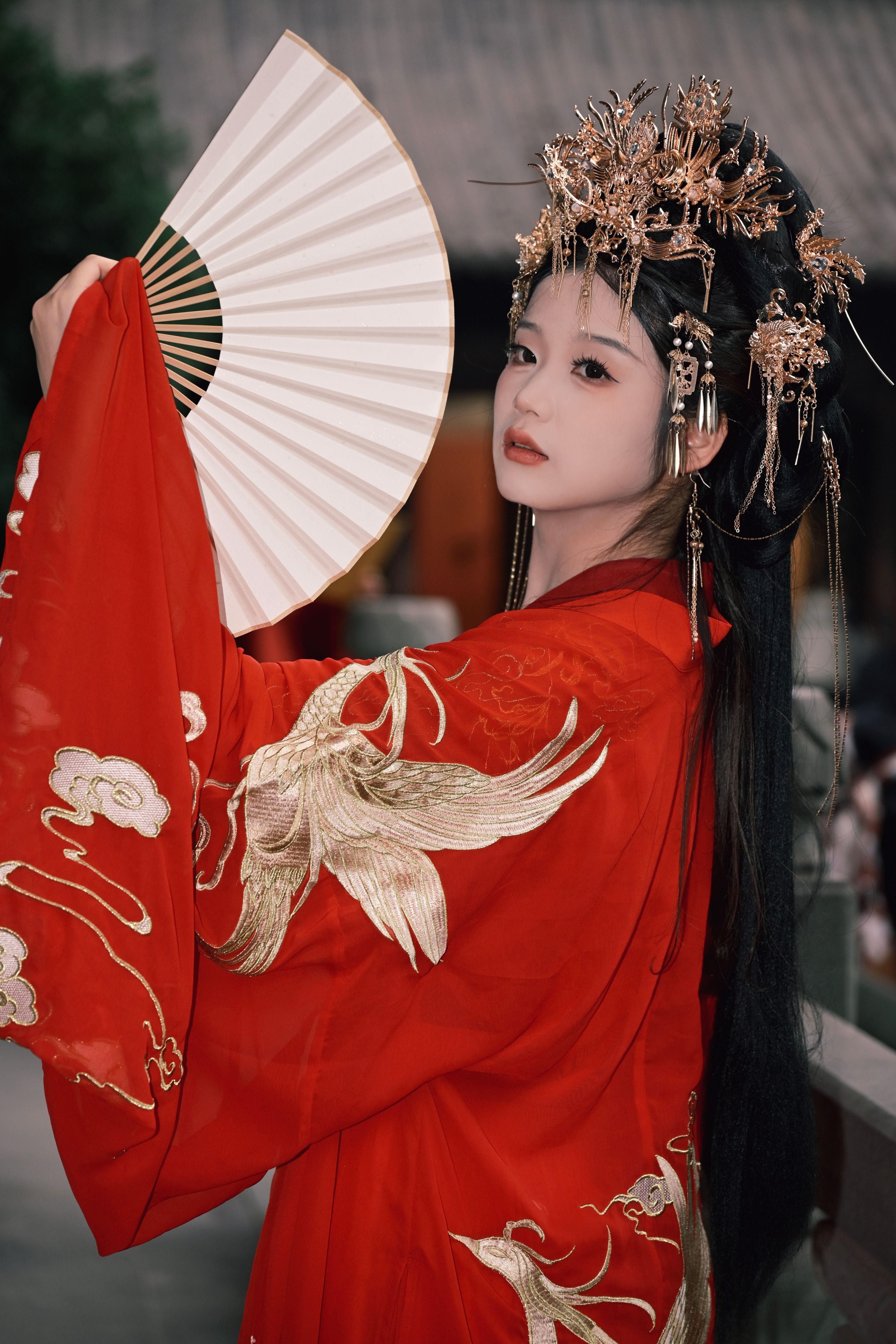 A woman elegantly dressed in a traditional red kimono with ornate hairpiece and holding a fan.