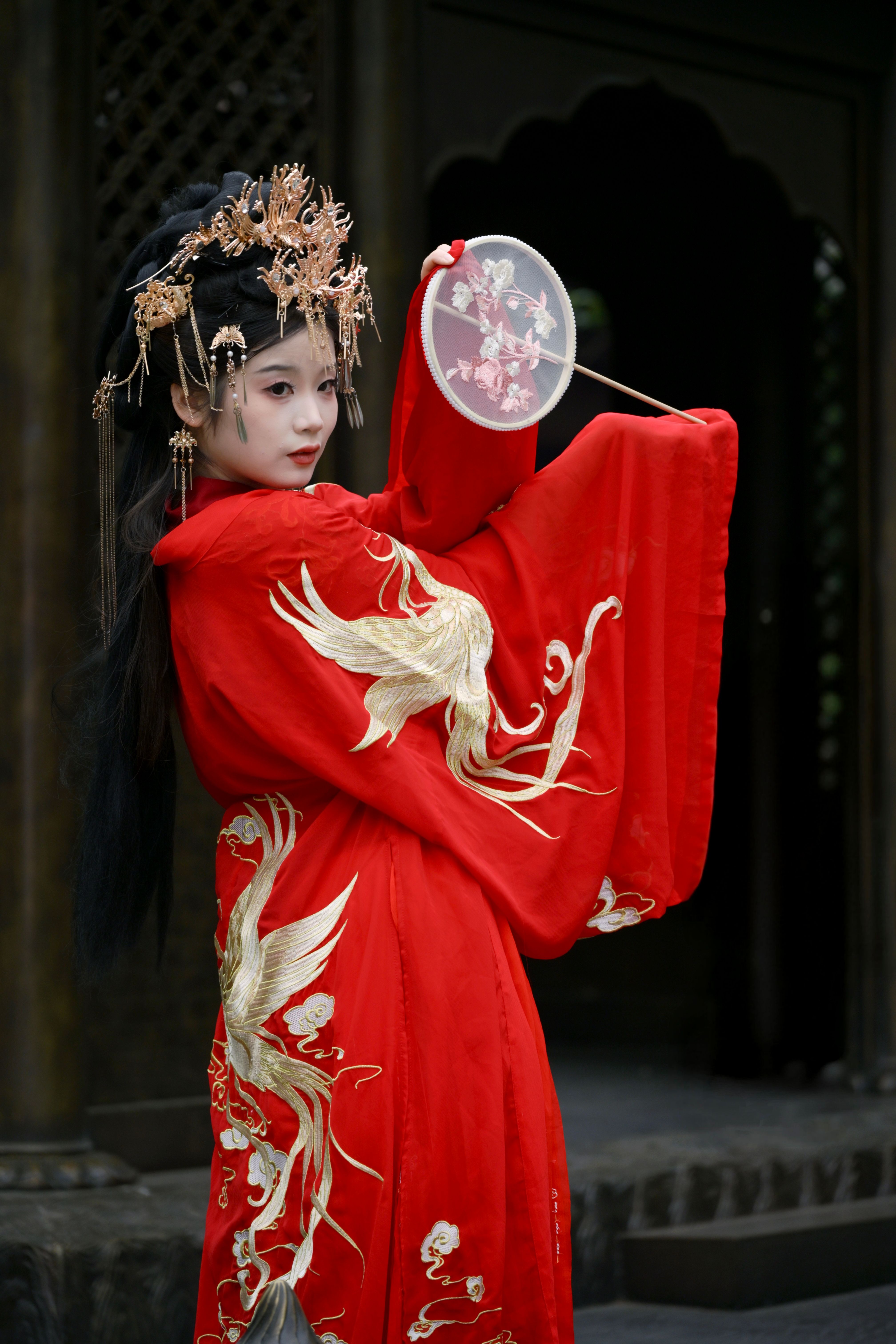 A woman elegantly poses in a traditional red gown with intricate gold designs.