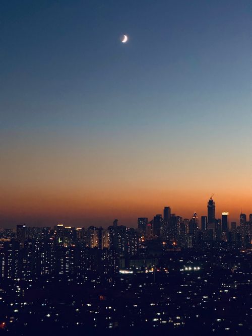 Free A mesmerizing view of a city skyline at twilight with a crescent moon above. Stock Photo