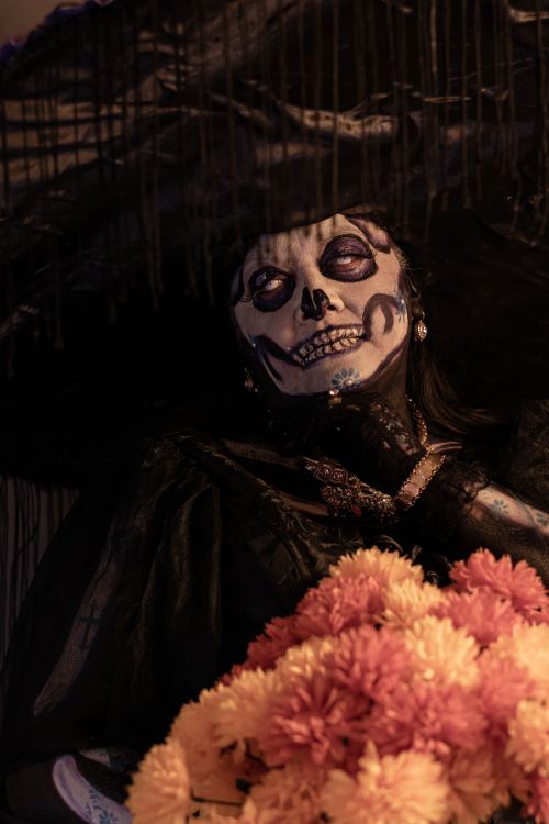 Free A woman in skull facepaint holding flowers during Day of the Dead celebration. Stock Photo