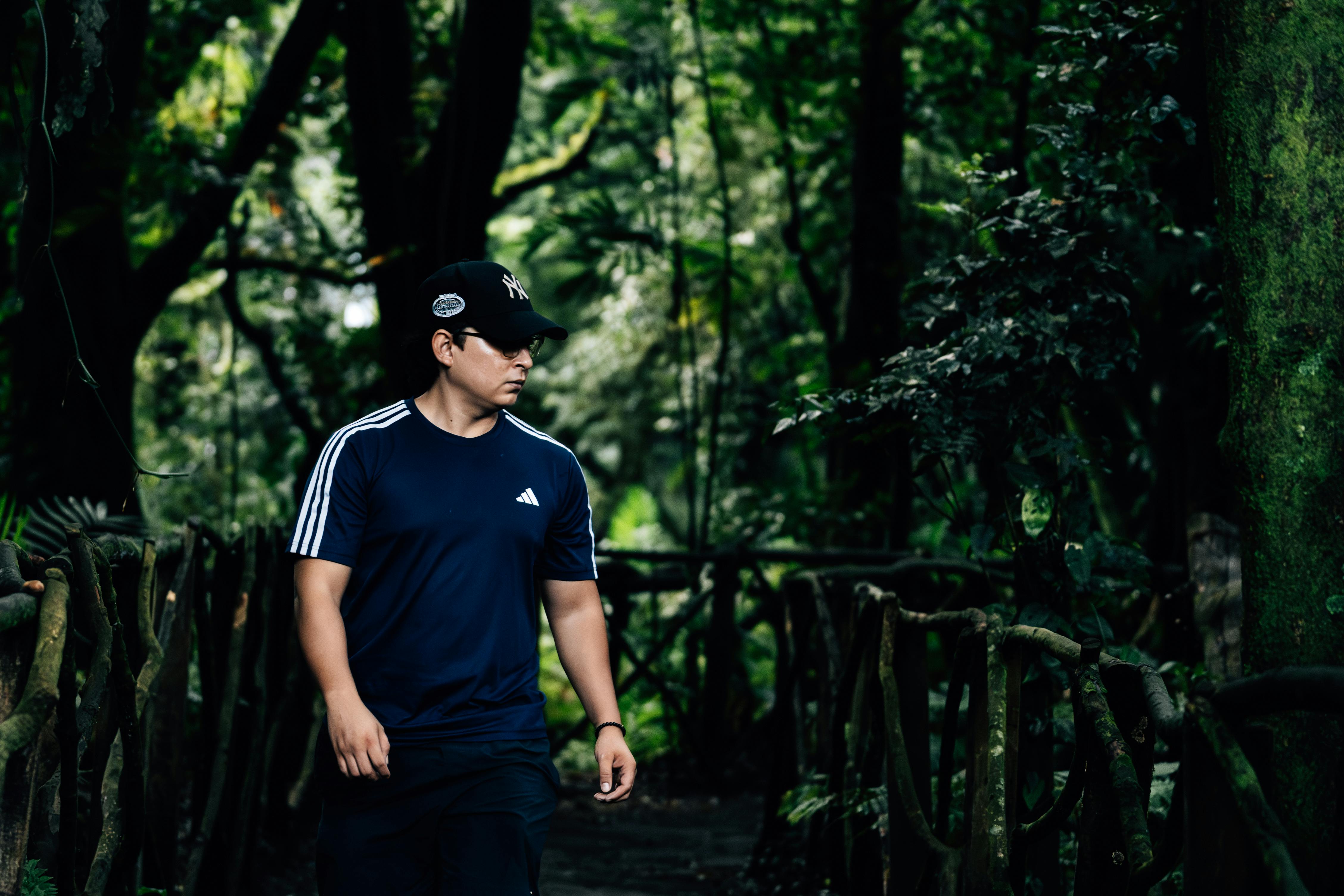 A man in athletic clothing walking through a lush, green forest path.