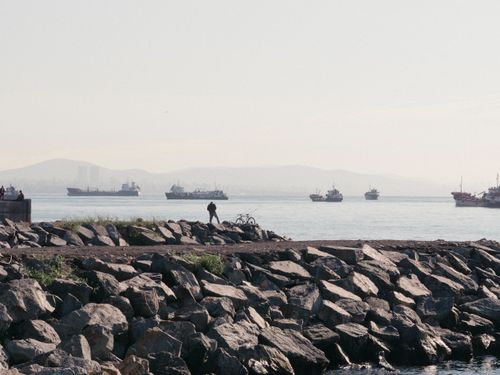 Free A tranquil coastal scene with ships on the horizon and a rocky shoreline in the foreground. Stock Photo