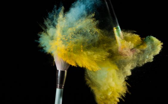 Vibrant colors of powder explode from brushes, creating a dynamic artistic effect against a black background.