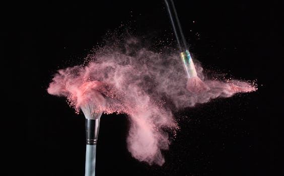 Close-up of makeup brushes colliding, releasing a cloud of pink powder against a black background.