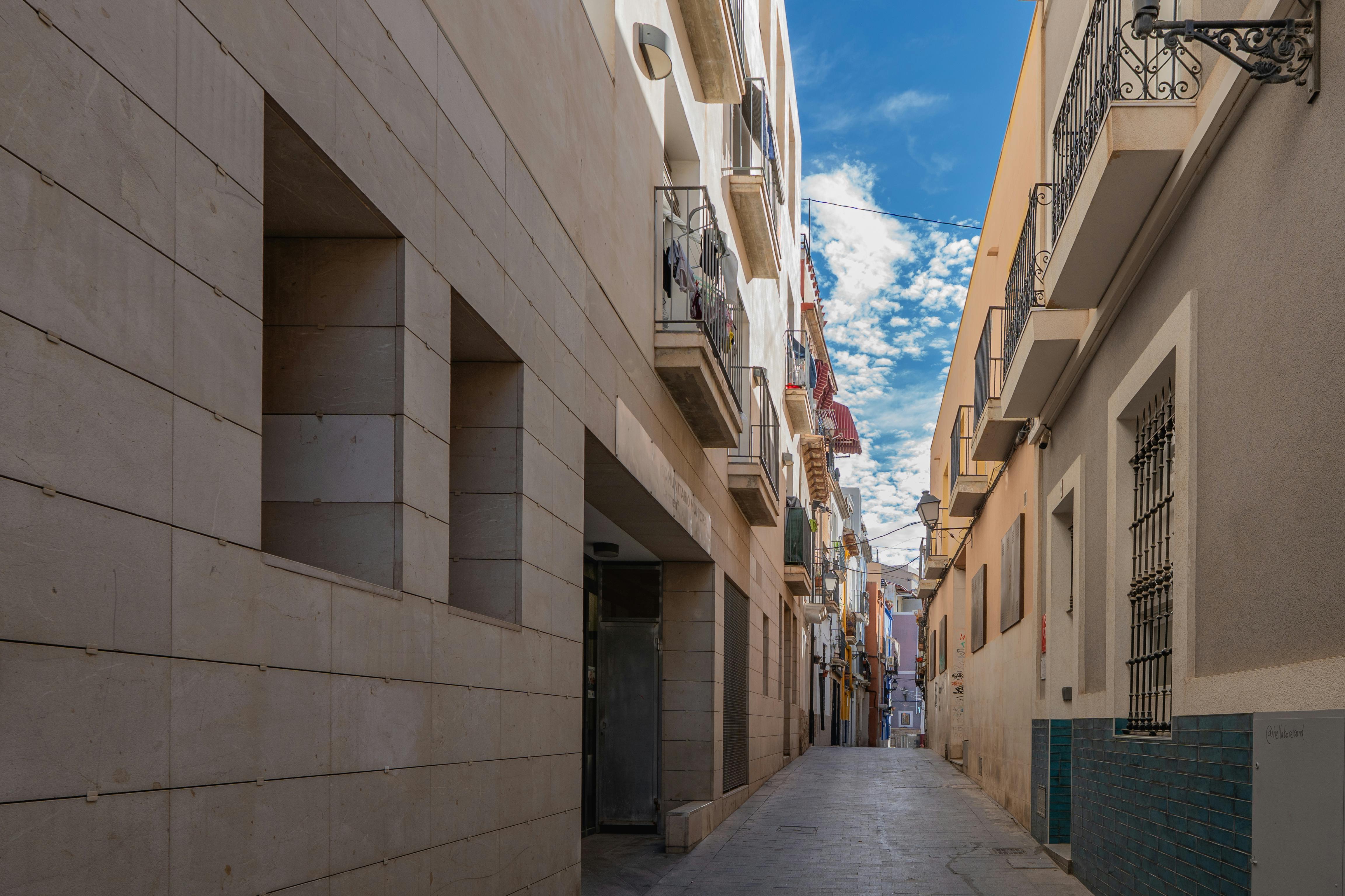 A scenic view of a narrow street with colorful buildings in Alicante, Spain under a clear blue sky.