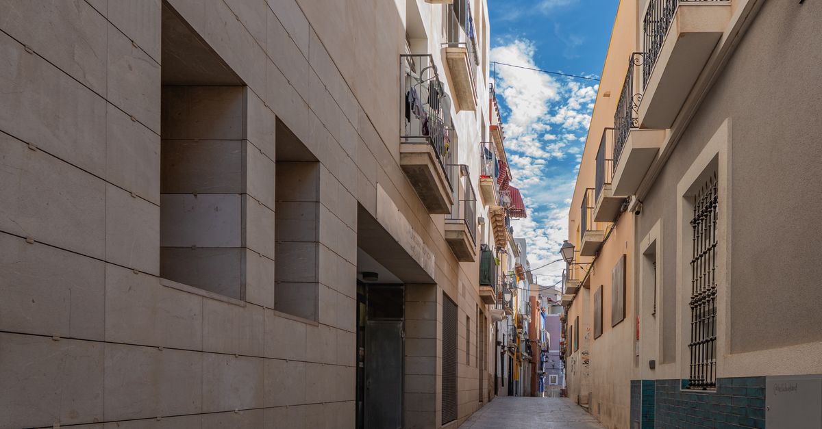 A scenic view of a narrow street with colorful buildings in Alicante, Spain under a clear blue sky.