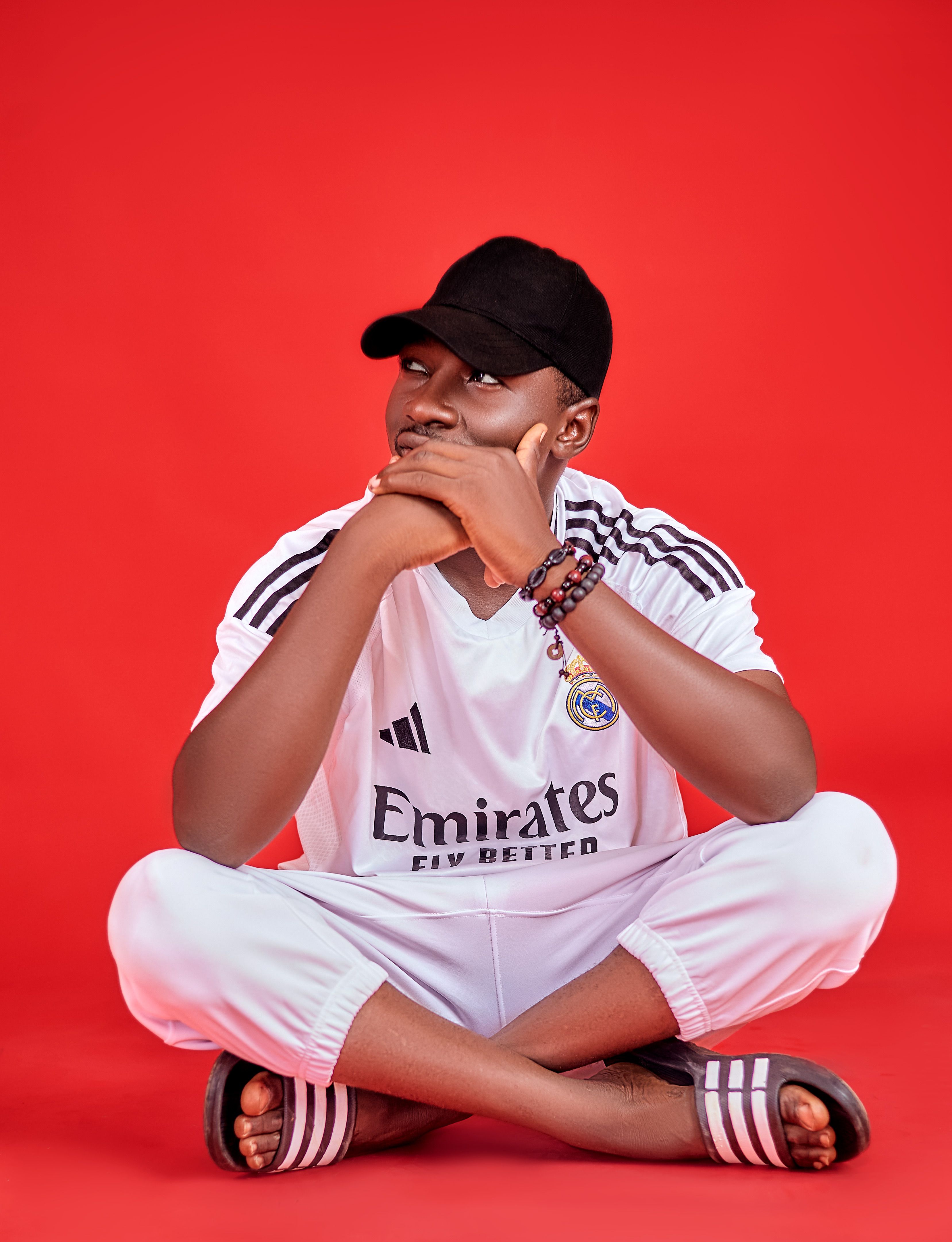 Man in Real Madrid jersey sitting on red background, relaxed pose.
